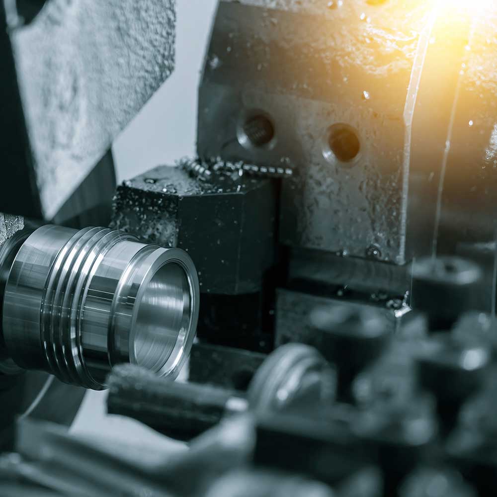 Tournage industriel d'une pièce métallique par une machine-outil. Copeaux d'acier. Lumière intense sur l'équipement de fabrication.